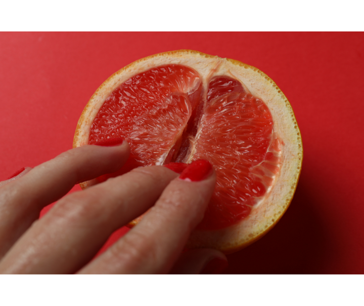 Main avec vernis à ongles rouge touchant un demi-pamplemousse sur fond rouge.